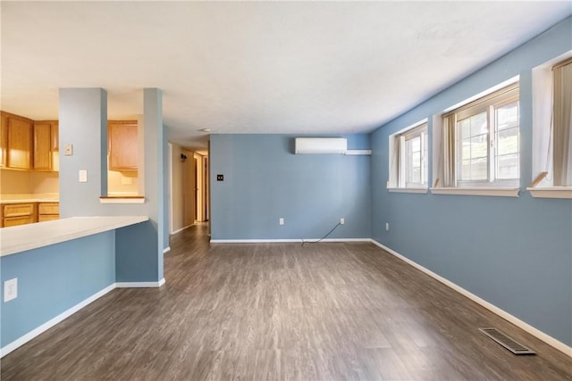 unfurnished living room featuring an AC wall unit, dark wood-type flooring, visible vents, and baseboards