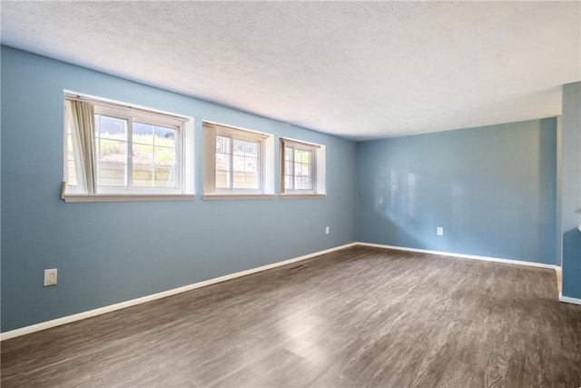 empty room featuring visible vents, a textured ceiling, baseboards, and dark wood-type flooring