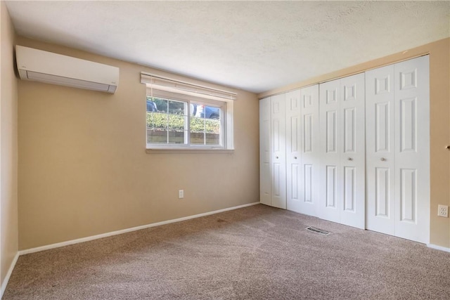 unfurnished bedroom featuring carpet floors, visible vents, an AC wall unit, a textured ceiling, and baseboards