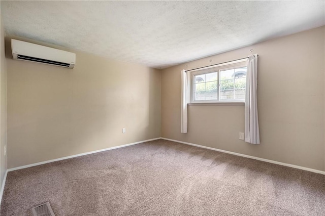 empty room featuring carpet floors, visible vents, a textured ceiling, a wall mounted air conditioner, and baseboards