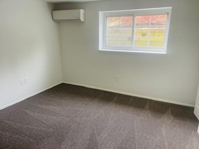 carpeted spare room featuring a wall mounted air conditioner and baseboards