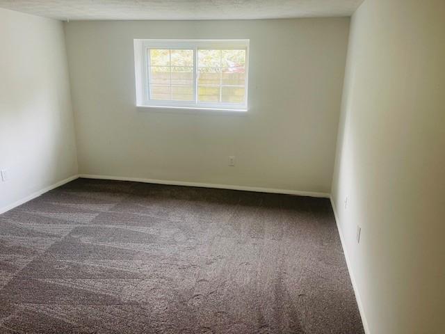 carpeted empty room with a textured ceiling and baseboards