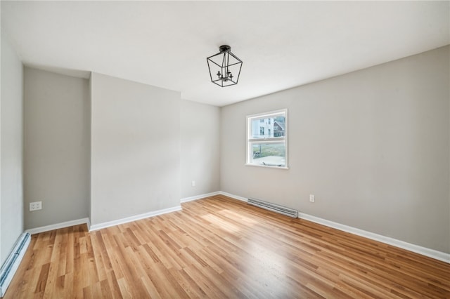 empty room featuring a baseboard radiator, a notable chandelier, and light hardwood / wood-style floors