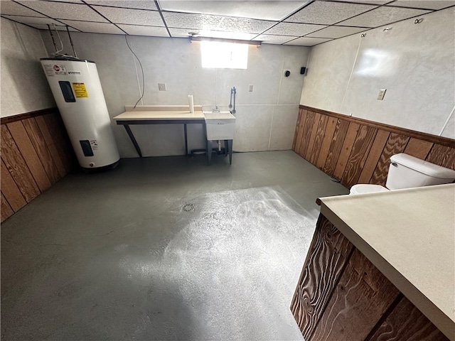 basement featuring electric water heater, sink, a paneled ceiling, and wooden walls