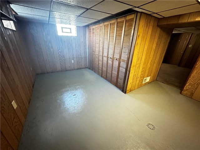 basement with wood walls and a drop ceiling