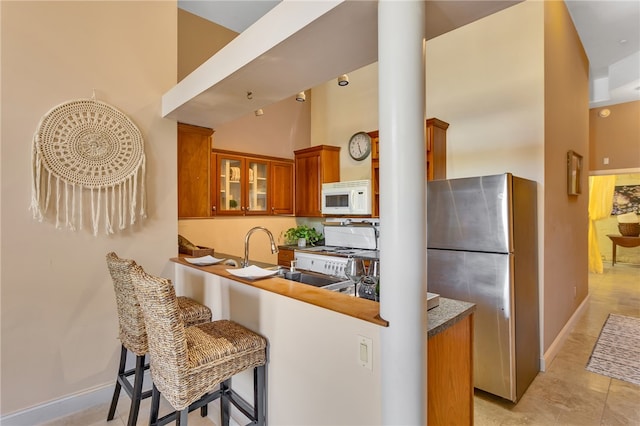 kitchen featuring kitchen peninsula, decorative columns, a kitchen breakfast bar, stainless steel refrigerator, and a high ceiling