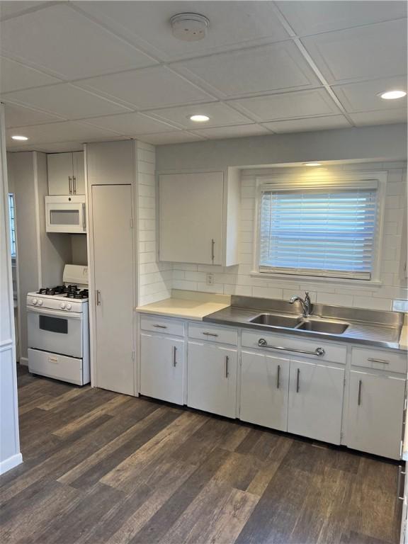 kitchen featuring dark wood finished floors, white appliances, backsplash, and a sink