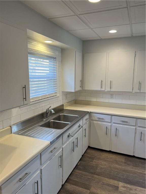 kitchen with a sink, backsplash, light countertops, white cabinetry, and dark wood-style flooring