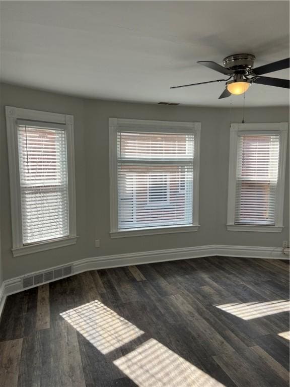 spare room featuring visible vents, plenty of natural light, baseboards, and wood finished floors