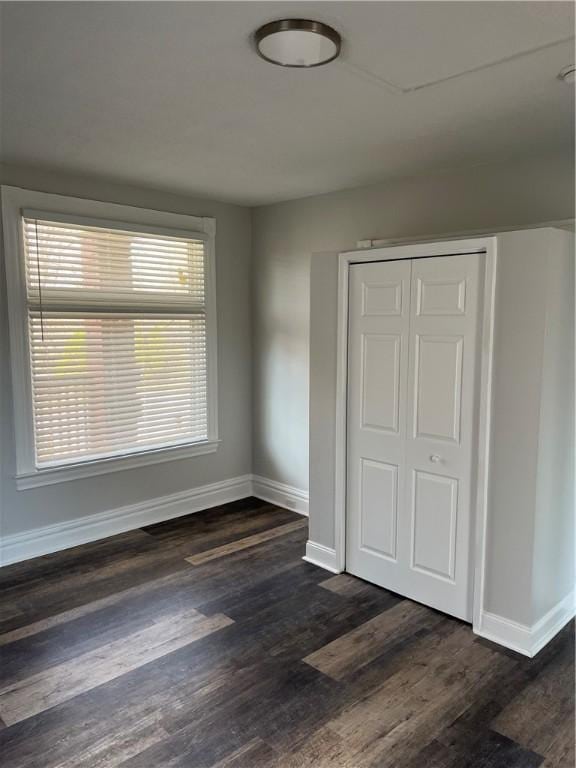 unfurnished bedroom with dark wood finished floors, baseboards, and a closet