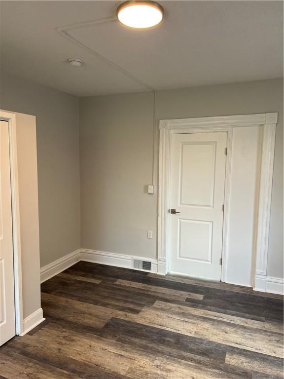 unfurnished room featuring dark wood-type flooring, visible vents, and baseboards