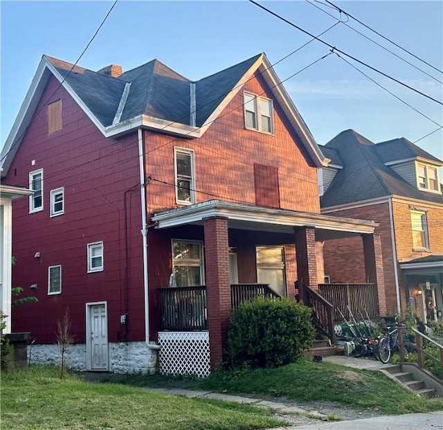 rear view of property with a porch, a chimney, and a yard