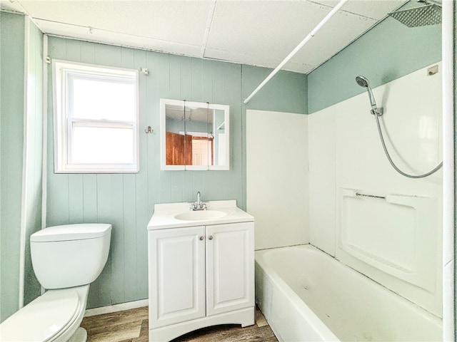 full bathroom with toilet, hardwood / wood-style floors, wooden walls, vanity, and washtub / shower combination