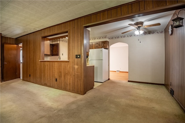 unfurnished room featuring ceiling fan, light carpet, and wooden walls