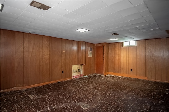 basement with a paneled ceiling, wood walls, and dark parquet floors