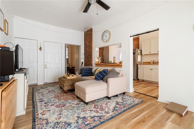 living room with ceiling fan, vaulted ceiling, and light hardwood / wood-style flooring