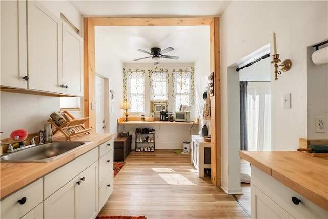 kitchen with ceiling fan, wooden counters, white cabinetry, and a sink