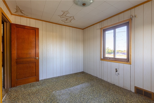 empty room featuring crown molding and wooden walls