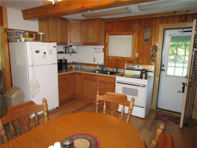 kitchen featuring light wood-type flooring, wood walls, white appliances, and sink