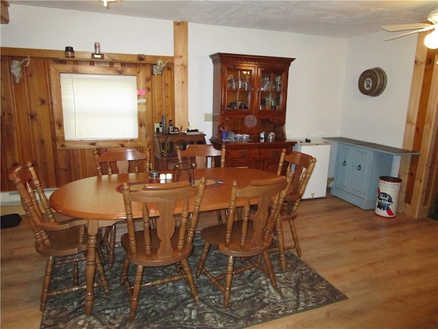 dining space featuring ceiling fan, hardwood / wood-style flooring, wooden walls, and a textured ceiling