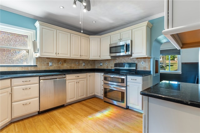 kitchen with appliances with stainless steel finishes, crown molding, tasteful backsplash, and light hardwood / wood-style floors