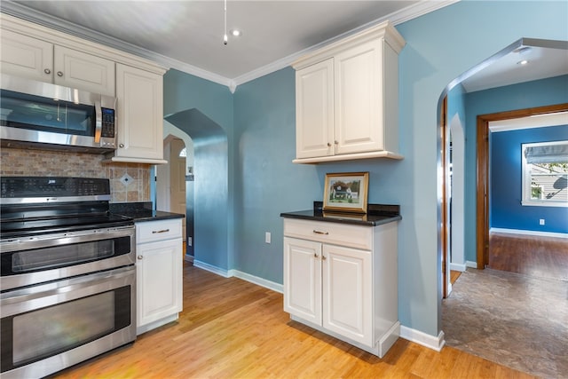 kitchen featuring appliances with stainless steel finishes, crown molding, decorative backsplash, and light wood-type flooring