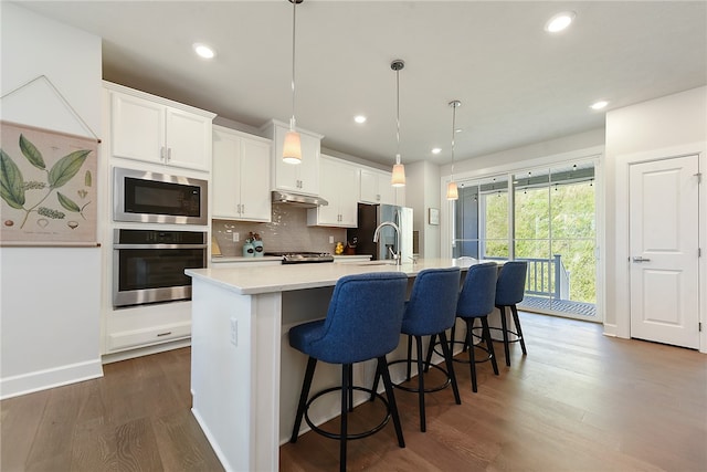 kitchen featuring appliances with stainless steel finishes, dark hardwood / wood-style flooring, a center island with sink, and white cabinets