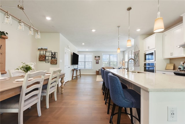 kitchen featuring white cabinets, hanging light fixtures, hardwood / wood-style floors, light stone countertops, and stainless steel appliances