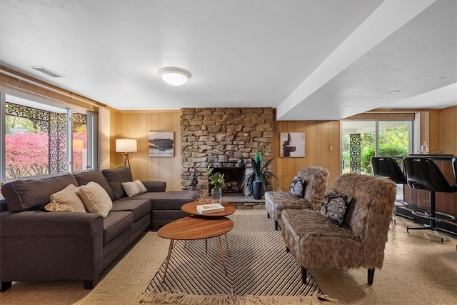 carpeted living room featuring a stone fireplace, wood walls, and a healthy amount of sunlight