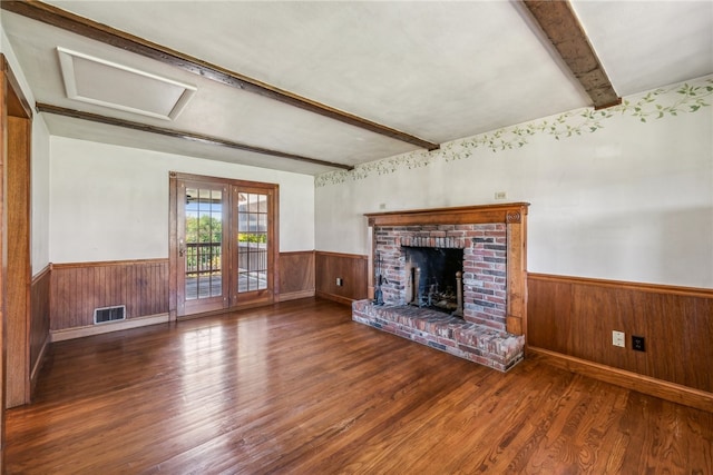 unfurnished living room with dark wood-type flooring, a brick fireplace, wood walls, and beamed ceiling