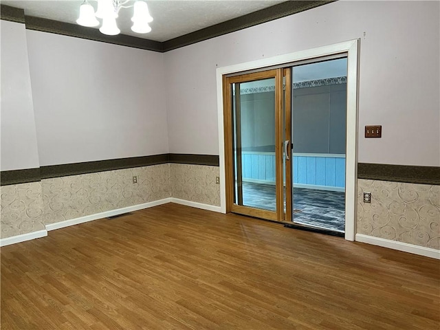 spare room with wood finished floors, visible vents, wallpapered walls, an inviting chandelier, and wainscoting