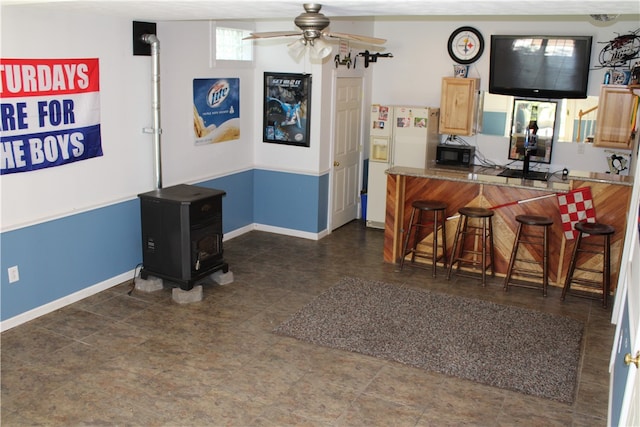 kitchen featuring white refrigerator with ice dispenser, kitchen peninsula, a breakfast bar area, a wood stove, and ceiling fan