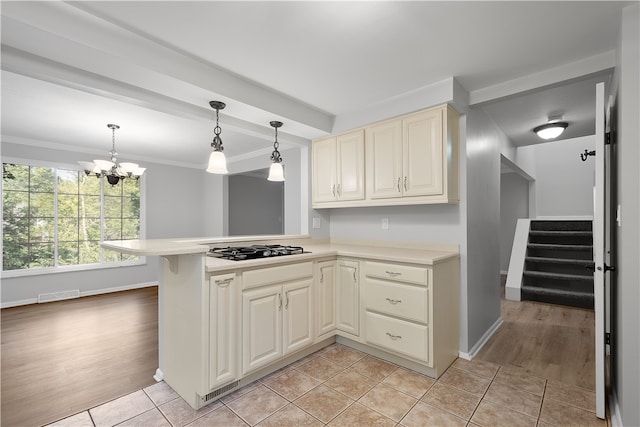 kitchen with light wood-type flooring, cream cabinets, decorative light fixtures, and stainless steel gas cooktop