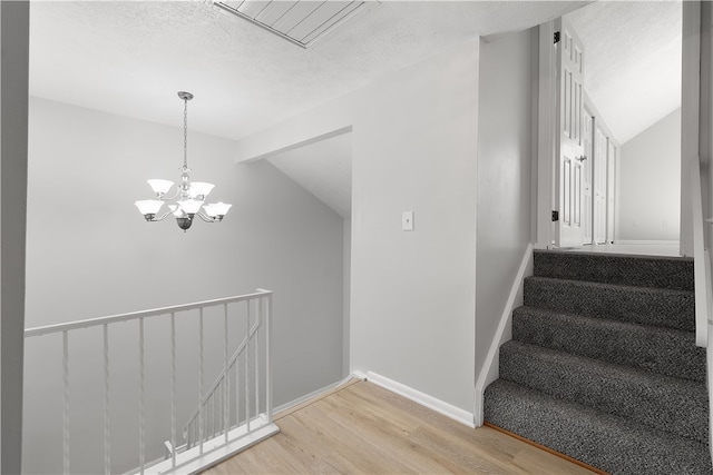 staircase featuring hardwood / wood-style floors, a notable chandelier, lofted ceiling with beams, and a textured ceiling