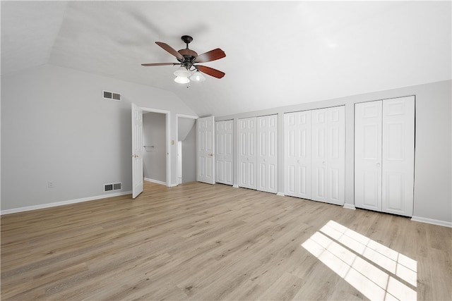 unfurnished bedroom with vaulted ceiling, ceiling fan, light wood-type flooring, and multiple closets