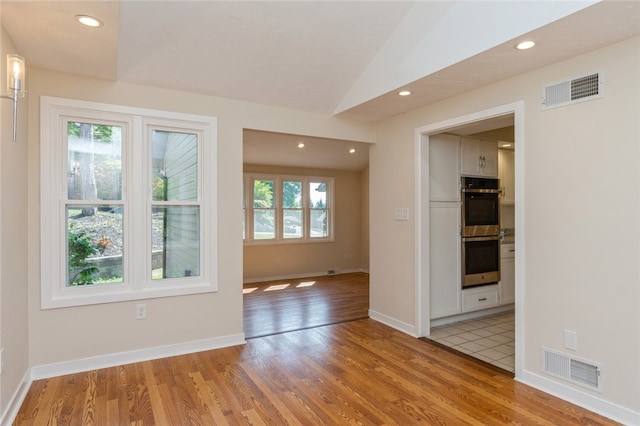 spare room with light hardwood / wood-style flooring, vaulted ceiling, and a healthy amount of sunlight