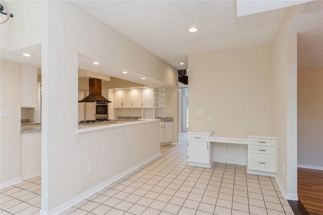 kitchen with wall chimney exhaust hood, white cabinetry, and light tile patterned flooring