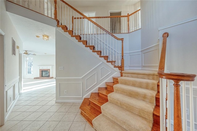 staircase with tile patterned floors, ceiling fan, a high ceiling, and a brick fireplace