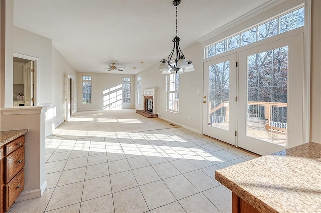 tiled living room featuring a fireplace, ceiling fan with notable chandelier, and a wealth of natural light