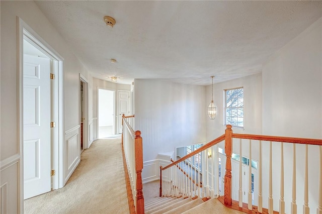 hallway with a textured ceiling, light carpet, and an inviting chandelier