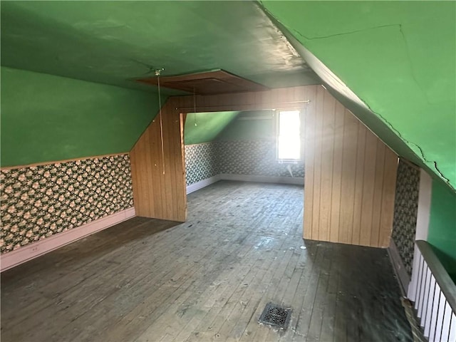 additional living space with lofted ceiling, wooden walls, visible vents, wood-type flooring, and baseboards