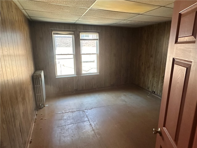 spare room featuring a paneled ceiling, wooden walls, and radiator heating unit