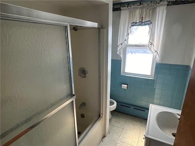 bathroom with baseboard heating, wainscoting, vanity, tile walls, and enclosed tub / shower combo