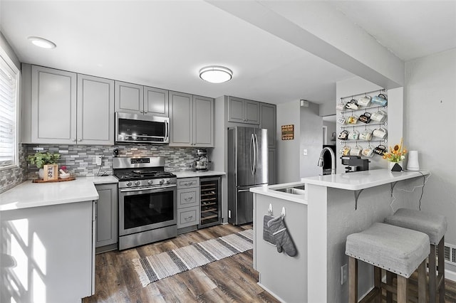 kitchen with a breakfast bar area, gray cabinetry, wine cooler, dark hardwood / wood-style flooring, and appliances with stainless steel finishes