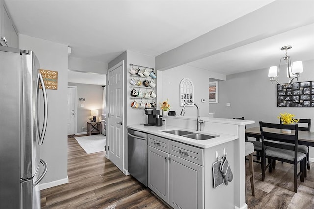 kitchen with pendant lighting, dark wood-type flooring, stainless steel appliances, sink, and a chandelier