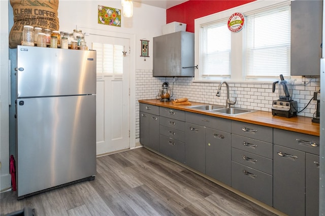 kitchen with wood counters, hardwood / wood-style floors, stainless steel refrigerator, sink, and tasteful backsplash