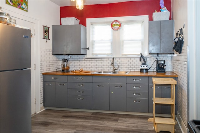 kitchen with dark wood-type flooring, wood counters, stainless steel refrigerator, and sink