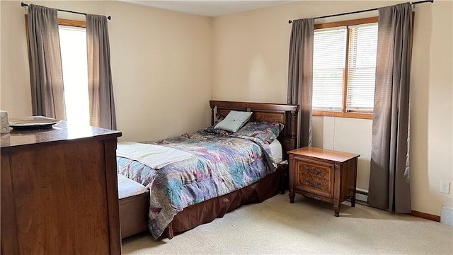 bedroom with multiple windows, light carpet, and a baseboard radiator