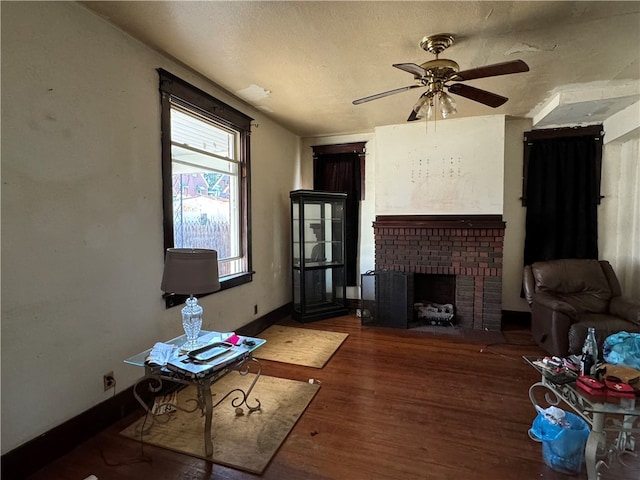 unfurnished living room with a textured ceiling, ceiling fan, hardwood / wood-style floors, and a brick fireplace