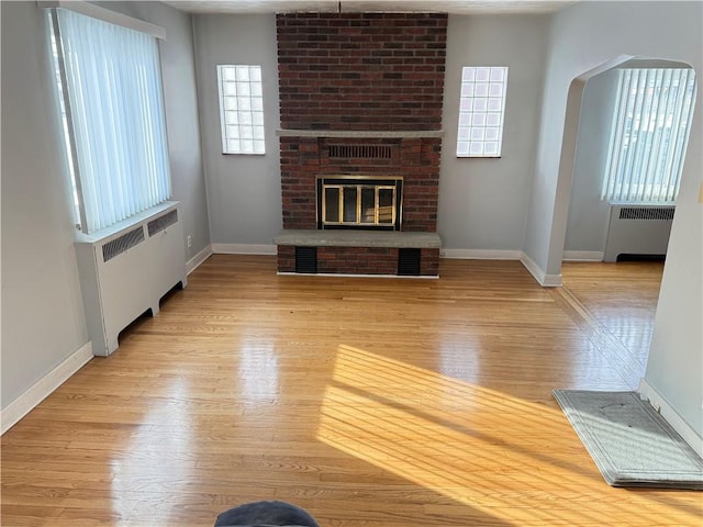 unfurnished living room featuring radiator, a brick fireplace, and light wood-type flooring